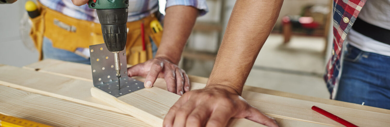 Man drilled a wooden plank and younger one helped